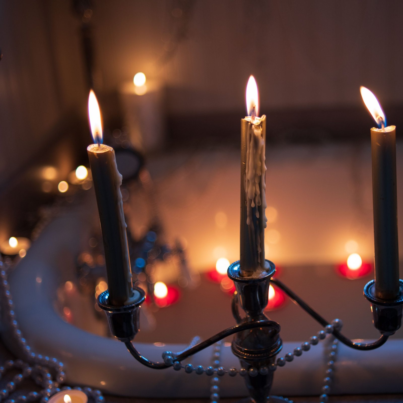 A serene candlelit atmosphere with burning candles and a candelabra near a luxurious bathtub.
